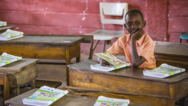 A Haitian elementary school student sits at his desk with a book, in a classroom setting